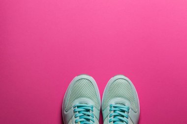 Pembe arka planda beyaz tabanlı turkuaz spor ayakkabılar.