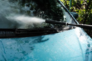 Evde tek başına araba yıka. Araba yıkama yüksek basınç yakın çekim. Bir adam yeşil bir arabayı yıkıyor..