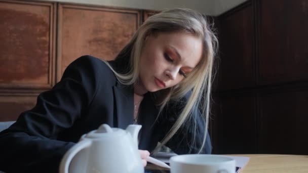 Una jovencita, una hermosa rubia se sienta en un café en las manos de una tableta. — Vídeo de stock