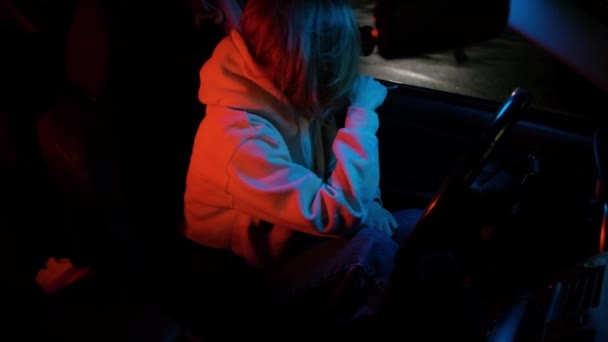 Una chica en un coche con un cigarrillo, sentada molesta y triste. Ciudad nocturna neón luz. — Vídeo de stock