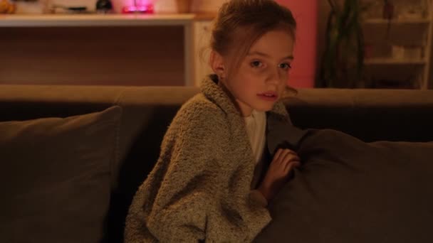 Uma menina assiste a um filme assustador e fica com medo. Um quarto à noite em um apartamento com uma TV. — Vídeo de Stock