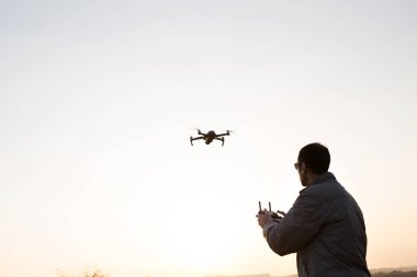 Bir adam gökyüzüne bir dron fırlatıyor. Batan güneşli İHA operatörü.