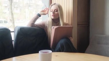 Elinde tabletle güzel bir sarışın. Kafede oturan bir kız tablete resim çiziyor..