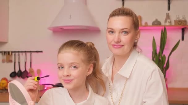Portret van moeder en dochter in de keuken thuis. Een volwassen meisje leert een klein meisje om cosmetica te gebruiken. — Stockvideo