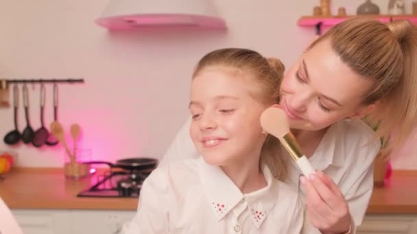Mamá enseña a su hija a usar cosméticos en la cocina luminosa por la noche. Maquillaje con un niño y un padre. — Vídeos de Stock