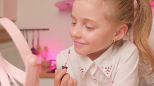 Porträt eines kleinen Mädchens in der heimischen Küche. Das Kind malt Lippen mit rosa Lippenstift und zwinkert. — Stockvideo