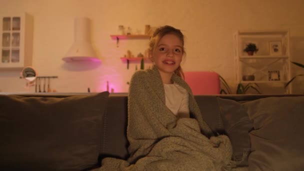 Portret van een kind in de avond in de kamer zit en kijkt TV en lacht. Het meisje kijkt een grappige film en is blij. — Stockvideo