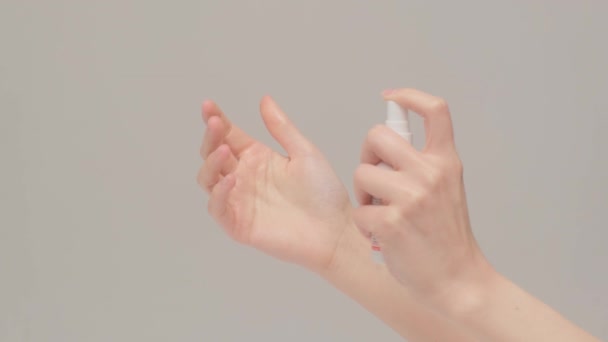 Женские руки применяют антисептик для личной гигиены. Фото сделано в студии на сером фоне — стоковое видео