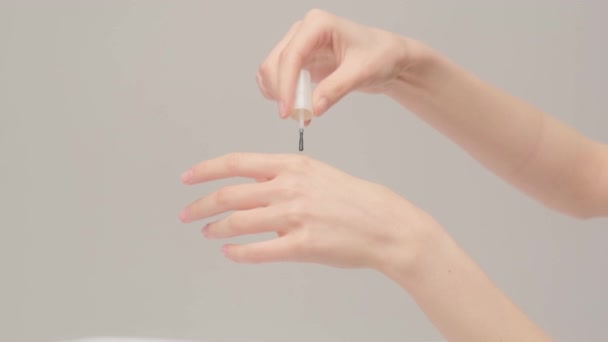 Close-up de mãos femininas durante a aplicação de óleo cosmético ou loção para restaurar a pele danificada e seca em um fundo cinza — Vídeo de Stock