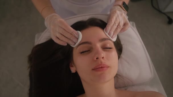 De schoonheidsspecialiste veegt de meisjes af met wattenstaafjes. Close-up portret van een huidverzorgingsprocedure. — Stockvideo