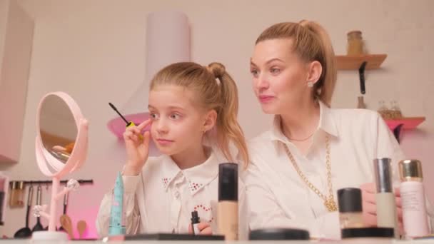 Mamá enseña a su hija a usar cosméticos en la cocina luminosa por la noche. Maquillaje con un niño y un padre. — Vídeos de Stock