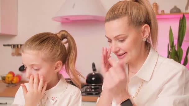 Mamá enseña a su hija a usar cosméticos en la cocina luminosa por la noche. Maquillaje con un niño y un padre. — Vídeo de stock