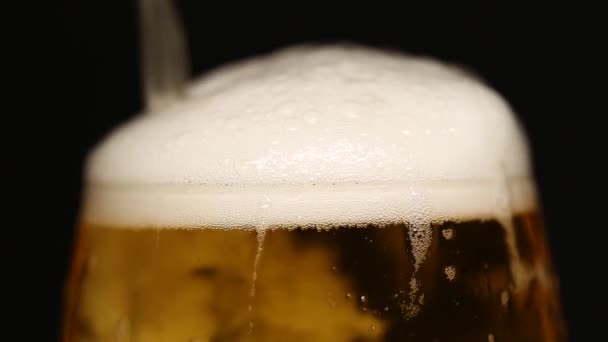 La espuma de cerveza se vierte sobre el borde en un primer plano de panadería. Fondo negro aislado. — Vídeo de stock