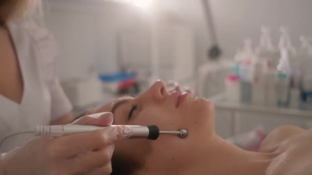 Procédures de soins de la peau du visage par un esthéticien. Thérapie microactuelle du visage d'une jeune belle fille. — Video