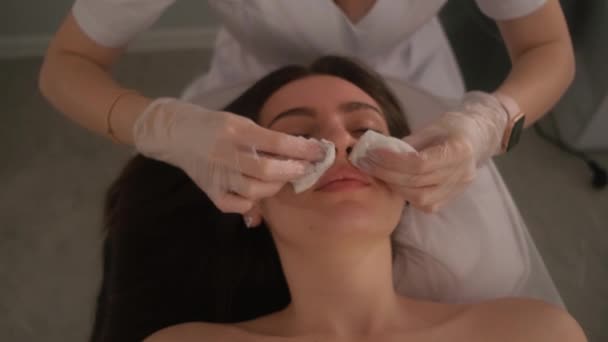 L'esthéticienne essuie le visage des filles avec des coton-tiges. Portrait en gros plan d'une procédure de soins de la peau. — Video