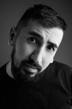 Gri arka planda sakallı genç bir adamın portresi. Genç adam gülümsüyor. Siyah beyaz fotoğraf.