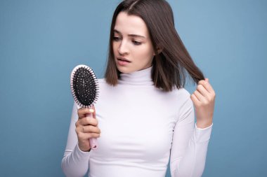 Elinde tarak olan bir esmer saç dökülmesinden endişe eder. Stüdyo resmi mavi arkaplan.