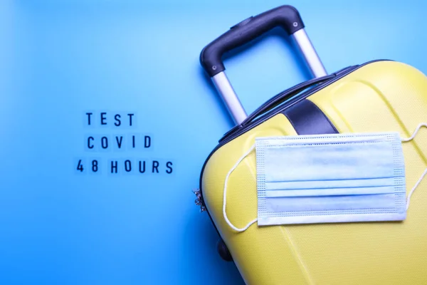 Luggage bag and mask on a blue background. Word test for covid 48 hours. Travel only with a covid test.