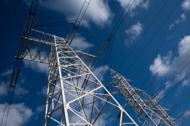 Mavi gökyüzünün arka planında bulutlu bir elektrik hattı kulesi.