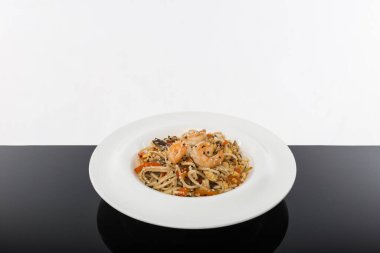 Siyah bir masada beyaz arka planı olan deniz mahsullü erişte.