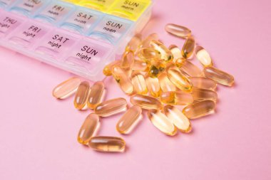 Organizer for medical pills on a pink isolated background close-up. Organization of taking pills of the day. Transparent vitamins lie nearby. clipart