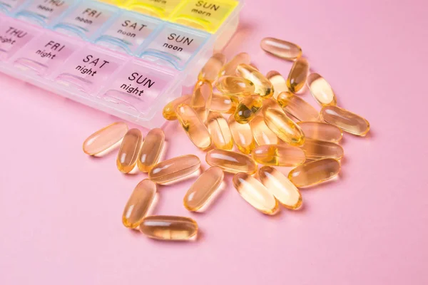 Организатор медицинских таблеток на розовом изолированном фоне крупным планом. Организация приема таблеток дня. Прозрачные витамины лежат поблизости. — стоковое фото