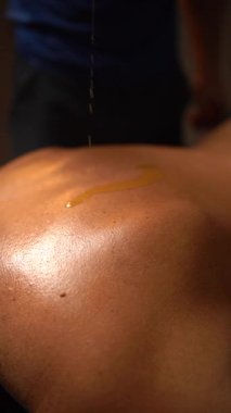 Erkek bir terapistin, rahatlatıcı bir spa tedavisinden önce bir kadına sıcak masaj yağı dökmesi..