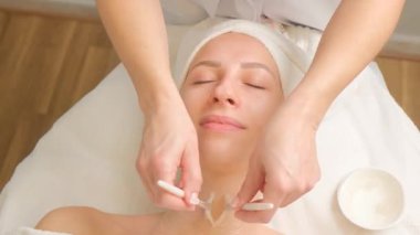 Güzellik salonunda profesyonel yüz bakımı alan bir kadının, fırça kullanarak cilt bakımı, rahatlama, kendine bakım ve modern kozmetoloji kullanarak cilt bakımı yapan bir kozmetikçiyle yakın çekimi..