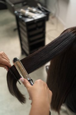 Profesyonel bir kuaför seansı sırasında saç düzleştirme sürecinin düz ütüsüyle yakın çekimi.