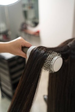 Güzellik salonunda pürüzsüz, parlak saçlar yaratan yuvarlak bir fırçayla saç şekillendirme sürecinin yakın çekimi.