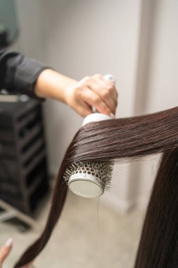 Güzellik salonunda pürüzsüz, parlak saçlar yaratan yuvarlak bir fırçayla saç şekillendirme sürecinin yakın çekimi.