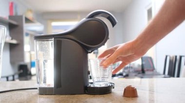 Kahve kapsülü makinesi içeceği hazırlarken bir el, modern bir mutfakta ya da ofiste cam bardağı damlalara koyar..