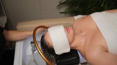 Kadın kuaförde saç yıkama ve kafa masajından zevk alıyor. Saç sağlığı ve rahatlama için profesyonel hidroterapi tedavisi