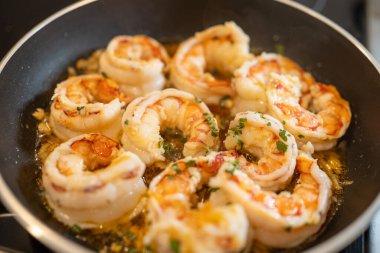 Sıcak tavada cızırdayan karides lezzetli bir yemek için taze maydanozlu sarımsaklı tereyağlı sos pişiriyor.