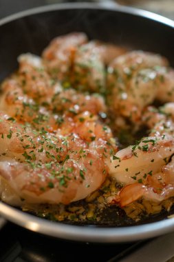 Zeytinyağlı karides sotesi, sarımsak ve maydanozla birlikte fırının üstünde taze, ev yapımı deniz ürünleri yemeği hazırlıyor.