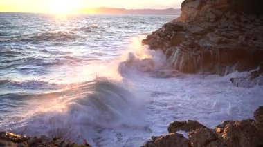 Kızgın deniz dalgaları dramatik bir günbatımında kayalıklarda kırılıyor. Muhteşem ve güçlü doğa muhteşem bir manzara yaratıyor.