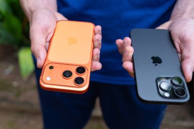 Tarragona, İspanya - 26 Ekim 2025: Elinde turuncu iPhone 16 Pro ve 17 Pro tutan bir adamın yakın çekimi.