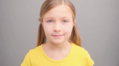 Gri bir arkaplanda gülümseyen sarı saçlı şirin bir kızın portresi.