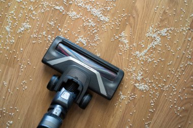 Tahta parke zeminden dökülen pirinci temizleyen elektrikli süpürge başı ev işlerini temsil ediyor.