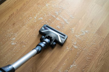 Elektrikli süpürge ev işleri sırasında ahşap zeminden dökülen pirinci topluyor.