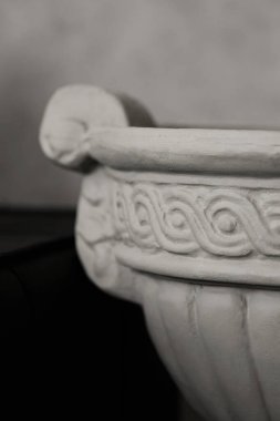 Klasik bir bahçe vazosu ya da vazonun dikey makro görüntüsü, siyah ve beyaz olarak sunuluyor. Görüntü, geleneksel bir Yunan dalga deseninin (Vitruvian parşömeni) yer aldığı dokulu yardım süslemesine odaklanır (Vitruvian parşömeni).)