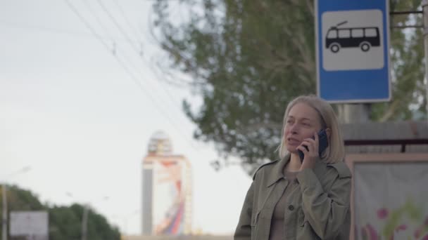 Eine Frau telefoniert an einer Bushaltestelle und lächelt
