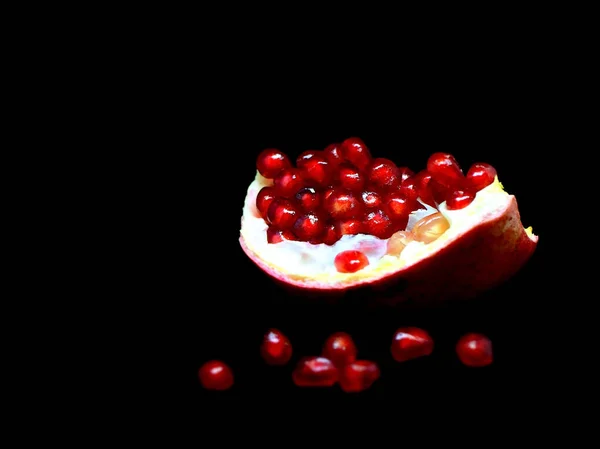 Slice the pomegranate with red grains on a black background, macro — Stock Photo, Image