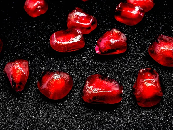 red grains of ripe pomegranate on a black background, narrow focus area, the grains Shine like a scattering of precious rubies or red garnets