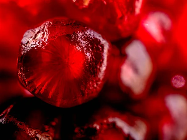 slice the pomegranate with red grains on a black background, a narrow focus area, surface texture of pomegranate seeds is visible