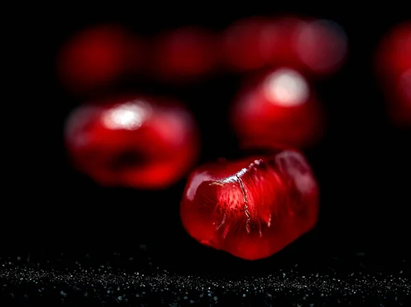 red grains of ripe pomegranate on a black background, narrow focus area, the grains Shine like a scattering of precious rubies or red garnets