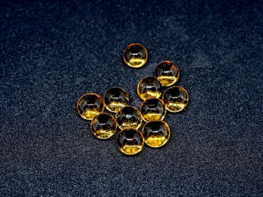 Sarı yuvarlak şeffaf jelatin kapsüller ve siyah arka planda balık yağı.