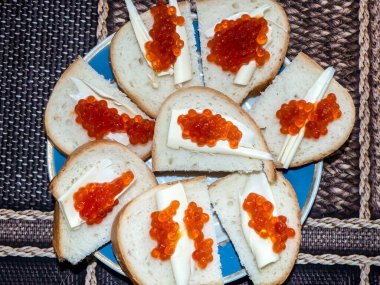 Beyaz ekmeğin üstünde kırmızı havyarlı sandviçler ve tereyağı tabakta.