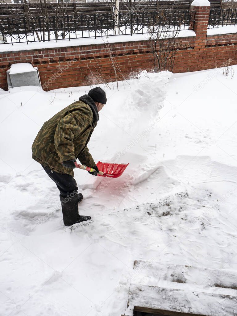 man removes fresh snow with a shovel during a snowfall