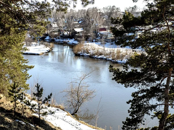 晴れた春の日には川の上流に松の木が生え川や村が見える距離で雪が溶け — ストック写真